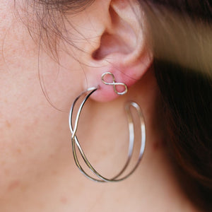 Close-up of a person wearing Infinity Hoops | Purpose Jewelry silver earrings featuring a small infinity symbol stud and a larger open hoop design, showcasing elegant minimalism.