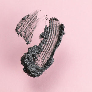 Close-up of textured black charcoal exfoliant product smear on a soft pink background, showcasing the gritty consistency of Down + Dirty™ Detoxifying Charcoal MicroExfoliant | ClarityRx for skincare.