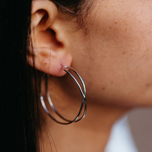 Close-up of a person wearing silver Infinity Hoops | Purpose Jewelry earrings, highlighting the delicate intertwined design against natural skin.
