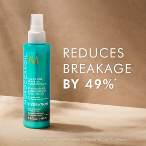 A turquoise bottle of All in One Leave-In Conditioner - Travel | Moroccanoil with a white spray cap standing on a wooden surface against a beige background with text highlighting its ability to reduce hair breakage by 49 percent.