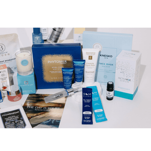 An assortment of skincare, body care, wellness supplements, and recovery tools arranged on a table featuring the 2026 Wellness Month Box ($1,140+ Value) | Live Love Spa.