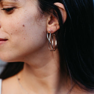 Close-up of a woman wearing silver Infinity Hoops | Purpose Jewelry earrings, showcasing the elegant twisted hoop design against her dark hair.