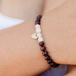 Close-up of a wrist wearing the Gemstone Heart Bracelet | Purpose Jewelry featuring dark red and white beads with a small gold heart charm.