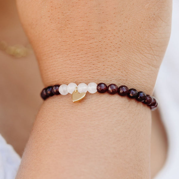 Close-up of a wrist wearing a Gemstone Heart Bracelet | Purpose Jewelry featuring dark red and white beads with a small gold heart charm, symbolizing elegance and intention.