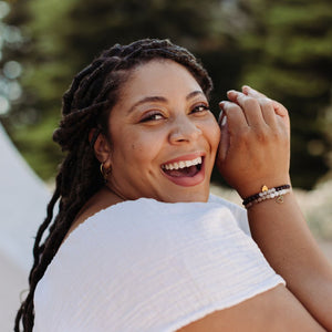 Smiling woman wearing the Gemstone Heart Bracelet | Purpose Jewelry with natural stone beads and a heart charm, showcasing a joyful and confident expression outdoors.