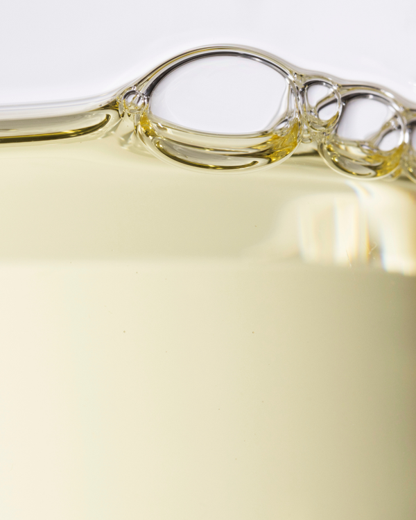 Close-up view of transparent golden liquid with bubbles, representing the Glow 49% Jojoba Oil Serum | Three Ships, a skincare product promoting natural hydration and wellness.