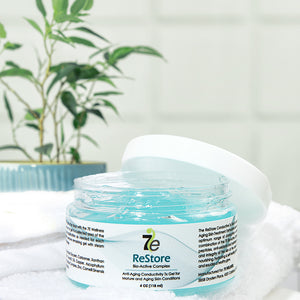 Open jar of ReStore Conductive Gel with Bio-Active Complex | 7e Wellness showing clear blue gel inside, placed on a white towel with a green plant in the background.