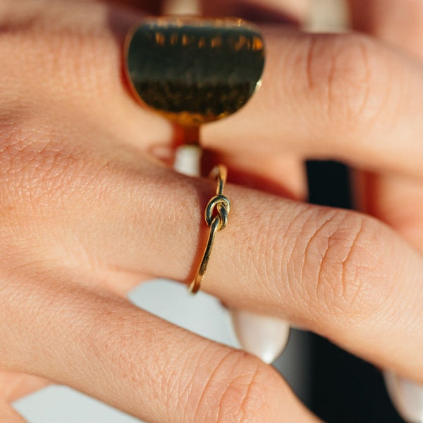 Close-up of a hand wearing a delicate gold Knot Ring | Purpose Jewelry, featuring a simple knot detail on a thin band.