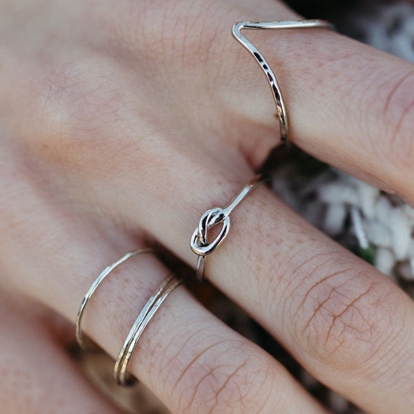 Close-up of a hand wearing three delicate silver rings including the Knot Ring | Purpose Jewelry, featuring a small knot design on a thin band.