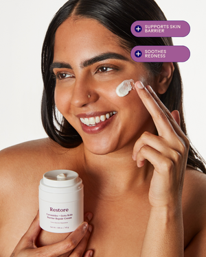 Happy woman applying Restore Ceramides + Gotu Kola Barrier Repair Cream | Three Ships on her cheek, promoting skin barrier support and soothing redness.