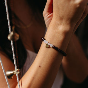 Close-up of a wrist wearing a Gemstone Heart Bracelet | Purpose Jewelry featuring dark and light beads with a small gold heart charm, styled with delicate accessories.