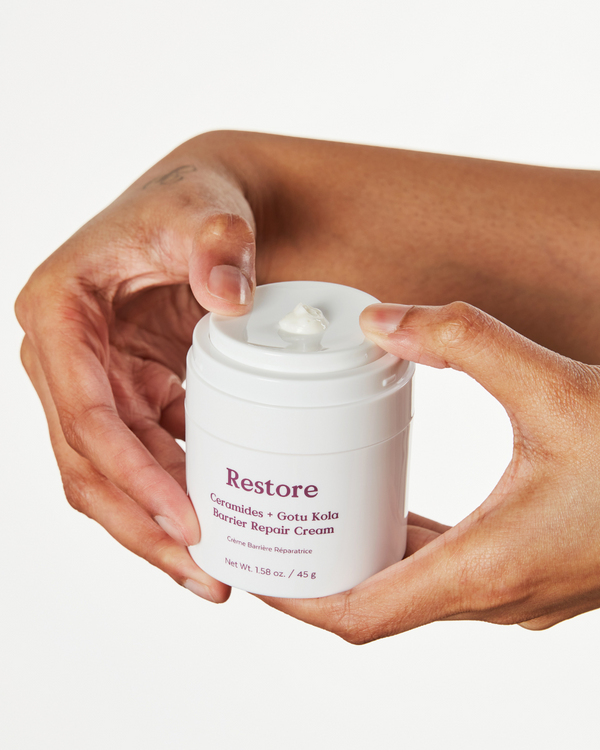 Hands holding a white jar of Restore Ceramides + Gotu Kola Barrier Repair Cream | Three Ships with a small amount of cream on the lid, showcasing skincare and body care wellness.