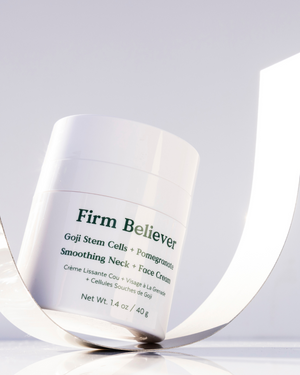 Jar of Firm Believer Goji Stem Cell + Pomegranate Smoothing Neck + Face Cream | Three Ships skincare product placed on a reflective surface with soft natural lighting.