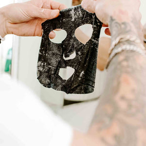 Hands holding a black facial sheet mask with cutouts for eyes, nose, and mouth, demonstrating use of the 7-Minute Makeover Mask | Skin Authority for skincare and wellness.
