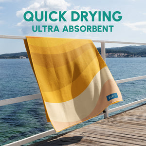 Waffle Microfiber Beach Towel - Boho | SUN'Y hanging on a railing by the water, showcasing its quick-drying and ultra-absorbent fabric in warm yellow and cream tones.