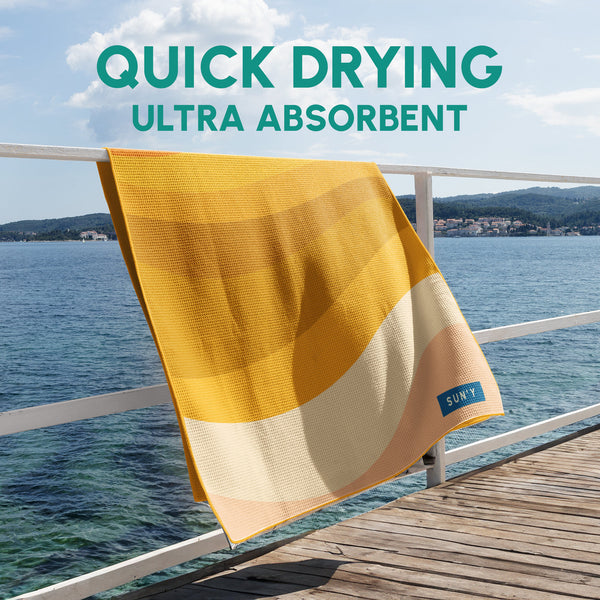Waffle Microfiber Beach Towel - Boho | SUN'Y hanging on a railing by the water, showcasing its quick-drying and ultra-absorbent fabric in warm yellow and cream tones.