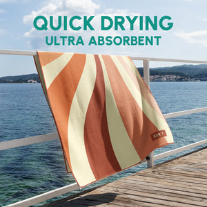 Waffle Microfiber Beach Towel - Rays | SUN'Y hanging on a railing by the water with bold orange and cream stripes, showcasing quick drying and ultra absorbent fabric.