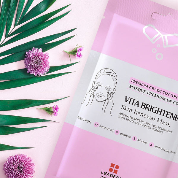 Pink and white packaging of Vita Brightening Skin Renewal Mask | Leaders beside green palm leaves and purple flowers, highlighting skincare and wellness themes.