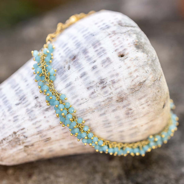 Delicate gold chain adorned with small aqua blue beads styled draped over a textured seashell, showcasing the Fringe Bracelet | Catherine Weitzman Jewelry.