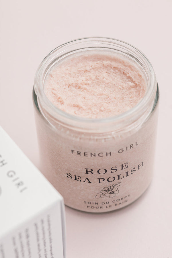 Open jar of Rose Body Polish | French Girl showing pale pink exfoliating scrub texture in clear container on a soft pink background, showcasing skincare and body care product for wellness.