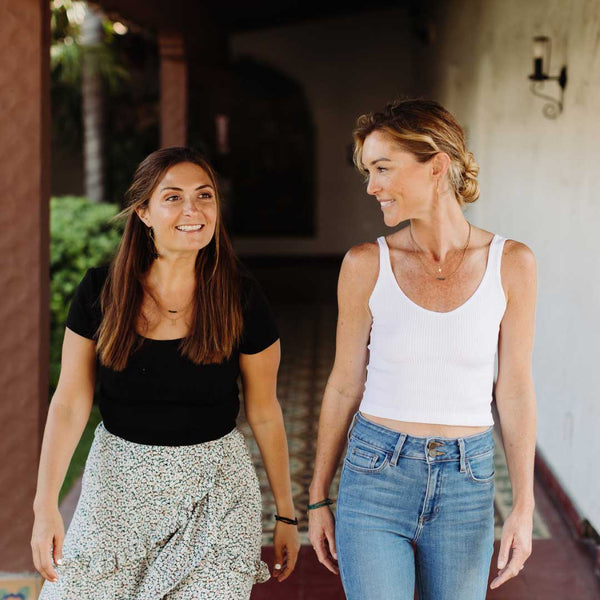 Two women walking and smiling outdoors, each wearing a Dusk Stretch Bracelet | Purpose Jewelry on their wrists, showcasing casual style and friendship.