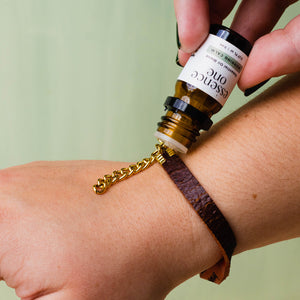 Hand applying Essential Oil Blends | Essence One onto a brown leather bracelet with a gold chain, highlighting a wellness and aromatherapy moment.