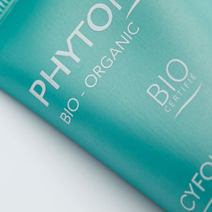 Close-up of a turquoise skincare tube displaying text including bio-organic certification, representing Cyfolia Organic - Radiance Exfoliating Cream | Phytomer for body care and skincare wellness.