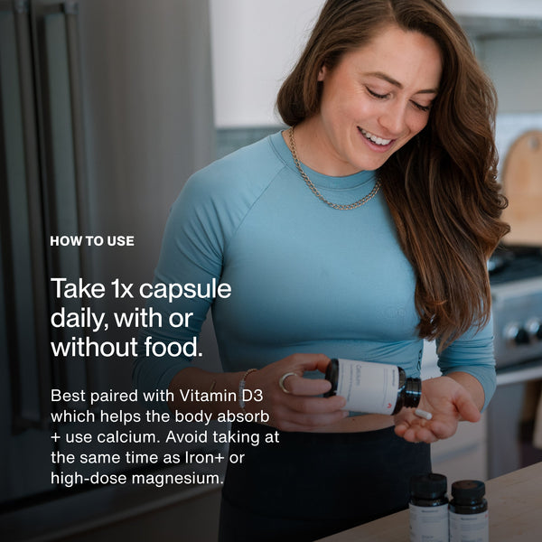 Woman in blue shirt smiling while holding a bottle of Calcium capsules with instructions on daily dosage and pairing advice for better absorption and use.