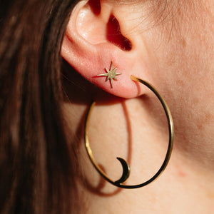 Close-up of an ear wearing a delicate gold star-shaped stud earring and a large gold hoop earring with a crescent moon detail, showcasing Galaxy Studs | Purpose Jewelry.
