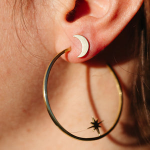 Close-up of an ear wearing crescent moon-shaped stud earrings and a large gold hoop earring with a star detail, showcasing Galaxy Studs | Purpose Jewelry.