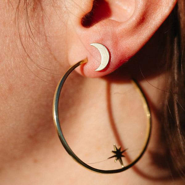 Close-up of an ear wearing crescent moon-shaped stud earrings and a large gold hoop earring with a star detail, showcasing Galaxy Studs | Purpose Jewelry.
