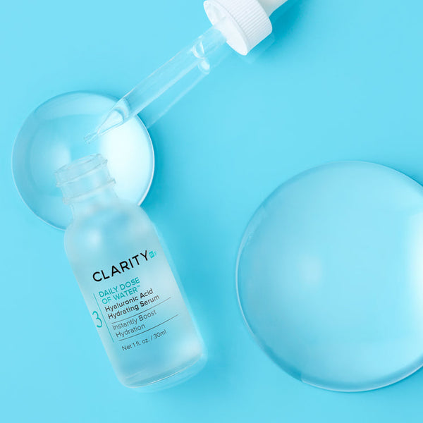 Clear frosted glass dropper bottle of Daily Dose Of Water™ Hyaluronic Acid Hydrating Serum | ClarityRx with serum drops and hydration droplets on a blue background for skincare hydration.