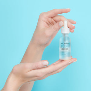 A pair of hands holding a frosted glass dropper bottle of Daily Dose Of Water™ Hyaluronic Acid Hydrating Serum | ClarityRx against a light blue background, showcasing skincare product and hydration benefits.