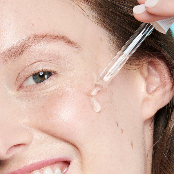 Close-up of a woman applying a clear drop of Daily Dose Of Water™ Hyaluronic Acid Hydrating Serum | ClarityRx to her cheek, showcasing skincare and hydration.