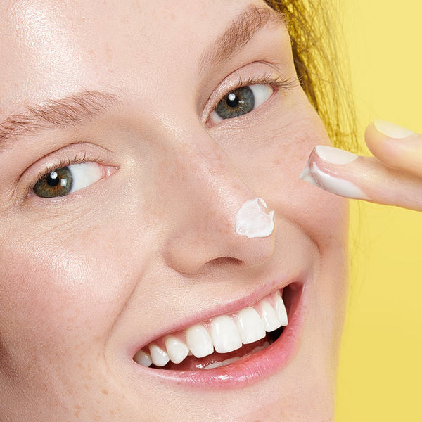 Close-up of a smiling woman with clear skin gently applying Feel Better™ Hyaluronic Acid Moisturizing Cream | ClarityRx to her nose, highlighting skincare and hydration.