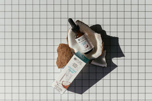 Coconut Water Infusion Drops | Pure Inventions bottle with dropper placed inside a halved coconut shell next to the product box on a grid-patterned surface, promoting wellness supplements.