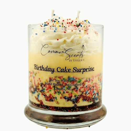Clear glass candle with layered cream and yellow wax, topped with whipped cream-like texture and colorful sprinkles, featuring "Dessert Candle | CommonScents by Tayler E" branding.
