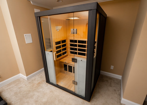 Modern infrared sauna cabin with wooden interior and glass door, designed for relaxation and wellness, featuring heating panels and ambient lighting, HaloSauna™ | Halotherapy Solutions.