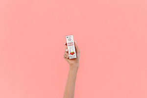 Hand holding a box of Super Fruit Extracts Water Infusion Drops - Cranberry + Elderberry | Pure Inventions against a soft pink background, highlighting wellness supplement packaging.