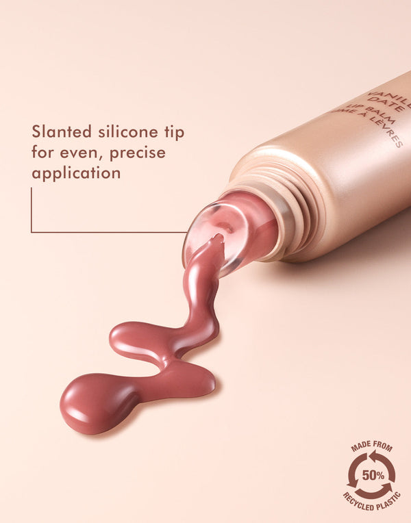 Close-up of Argan Butter Lip Balm | Moroccanoil with pinkish balm flowing from a tube featuring a slanted silicone tip for precise application, against a soft beige background.