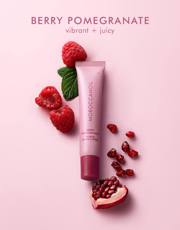 Argan Butter Lip Balm | Moroccanoil tube surrounded by raspberries, pomegranate seeds, and a green leaf on a pink background, highlighting vibrant and juicy berry pomegranate flavor for skincare.