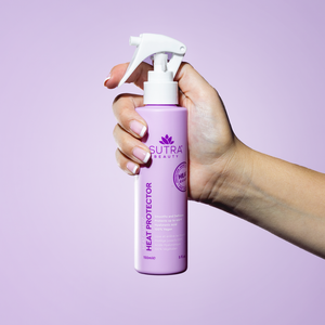 Hand holding a lavender spray bottle of Heat Guard Heat Protector | SUTRA against a light purple background, designed for hair care and protection with a sleek white spray nozzle.