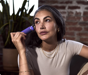 Woman using the Theraface Depuffing Wand | Therabody in a relaxed indoor setting, demonstrating a skincare routine focused on wellness and facial care.