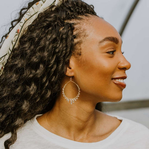 Woman with curly hair wearing a floral headband and elegant loop earrings from Desert Drops | Purpose Jewelry, showcasing a warm and natural profile look.