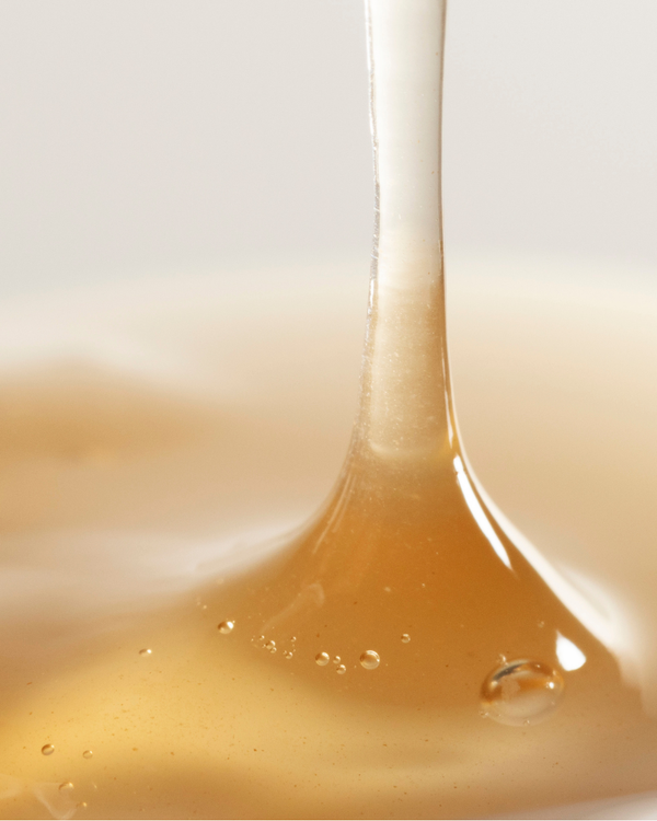 Close-up of golden hyaluronic acid serum being poured, showcasing smooth and glossy texture for Dew Drops Mushroom + Kakadu Plum Hyaluronic Acid Serum | Three Ships skincare product.