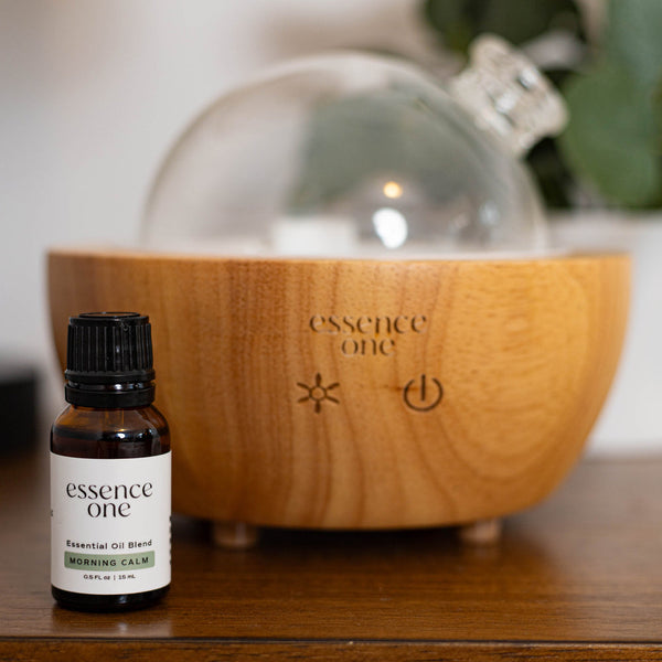 Essential Oil Blends | Essence One bottle labeled Morning Calm next to a wooden diffuser with soft natural lighting promoting wellness and relaxation.