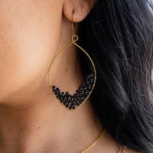 Close-up of a gold teardrop-shaped earring adorned with small black beads worn on an ear, showcasing the elegant design of Dusk Drops | Purpose Jewelry.