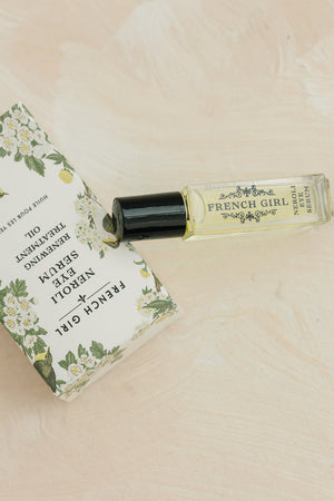 Glass roller bottle of Neroli Eye Serum | French Girl next to its floral-patterned box on a light beige surface, showcasing skincare and wellness aesthetics.