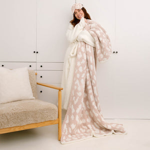 Woman wearing Eye Masks - Leopard - Chenilla Classic™ - O/S | Kashwére in a soft pink and cream leopard pattern while holding a matching cozy blanket in a minimalist white room.