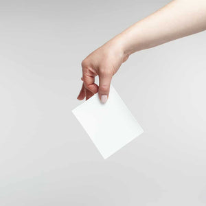Hand holding a single white Laundry Detergent Sheets | Force of Nature sheet against a plain light gray background.